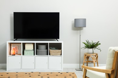 Modern TV on cabinet, armchair and beautiful houseplant indoors. Interior design