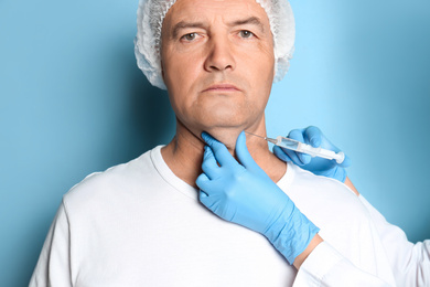 Photo of Mature man with double chin receiving injection on blue background