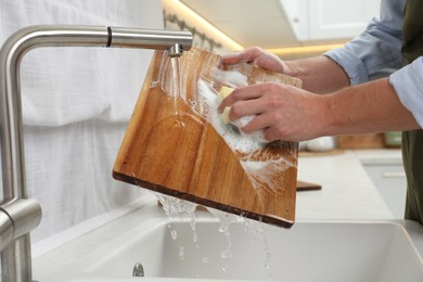 Photo of Man washing wooden cutting board in kitchen, closeup