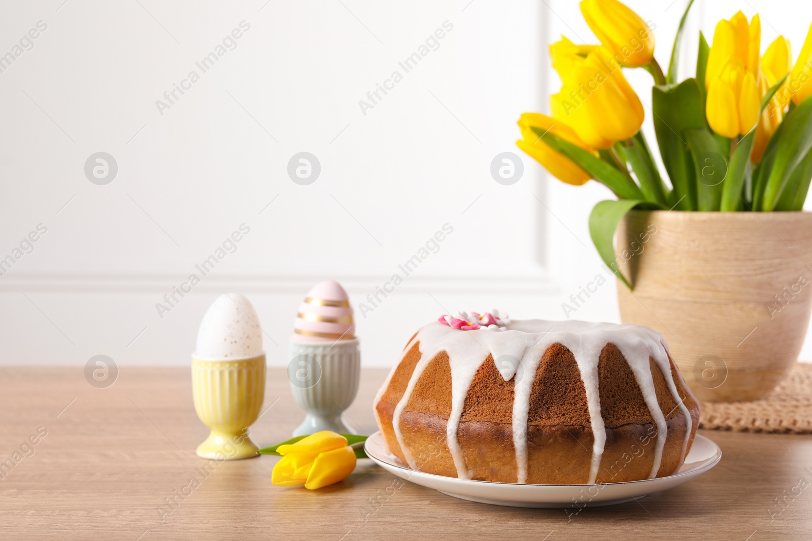 Photo of Delicious Easter cake decorated with sprinkles near beautiful tulips and painted eggs on wooden table. Space for text