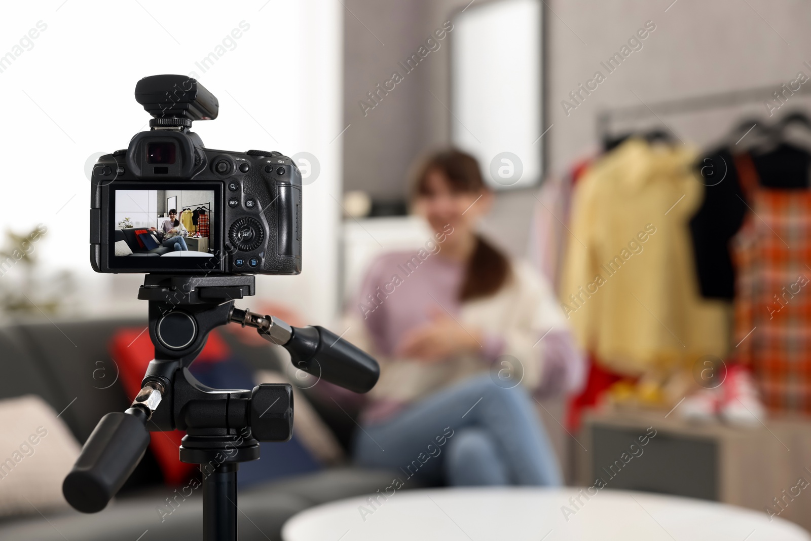 Photo of Fashion blogger explaining something while recording video at home, focus on camera