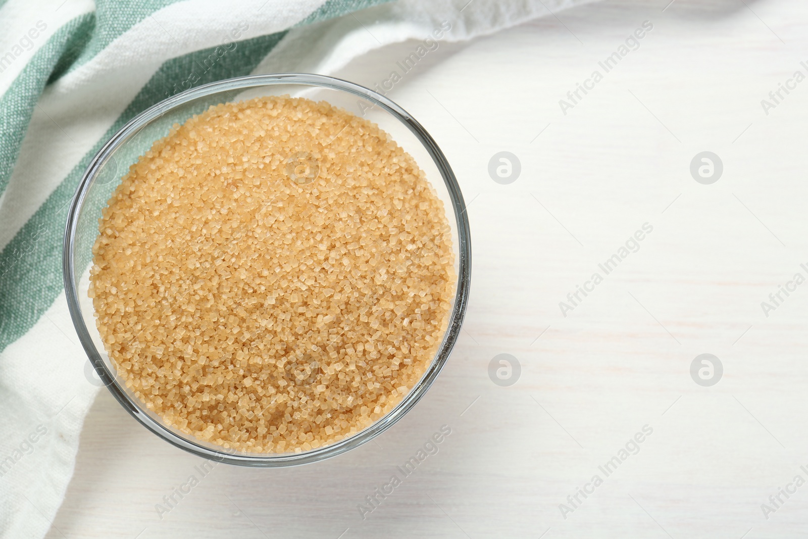 Photo of Brown sugar in glass bowl on white wooden table, top view. Space for text