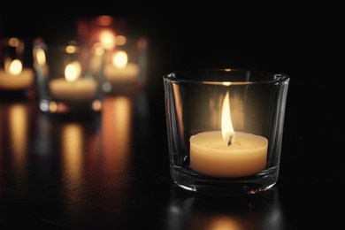 Burning candle on table in darkness, space for text. Funeral symbol