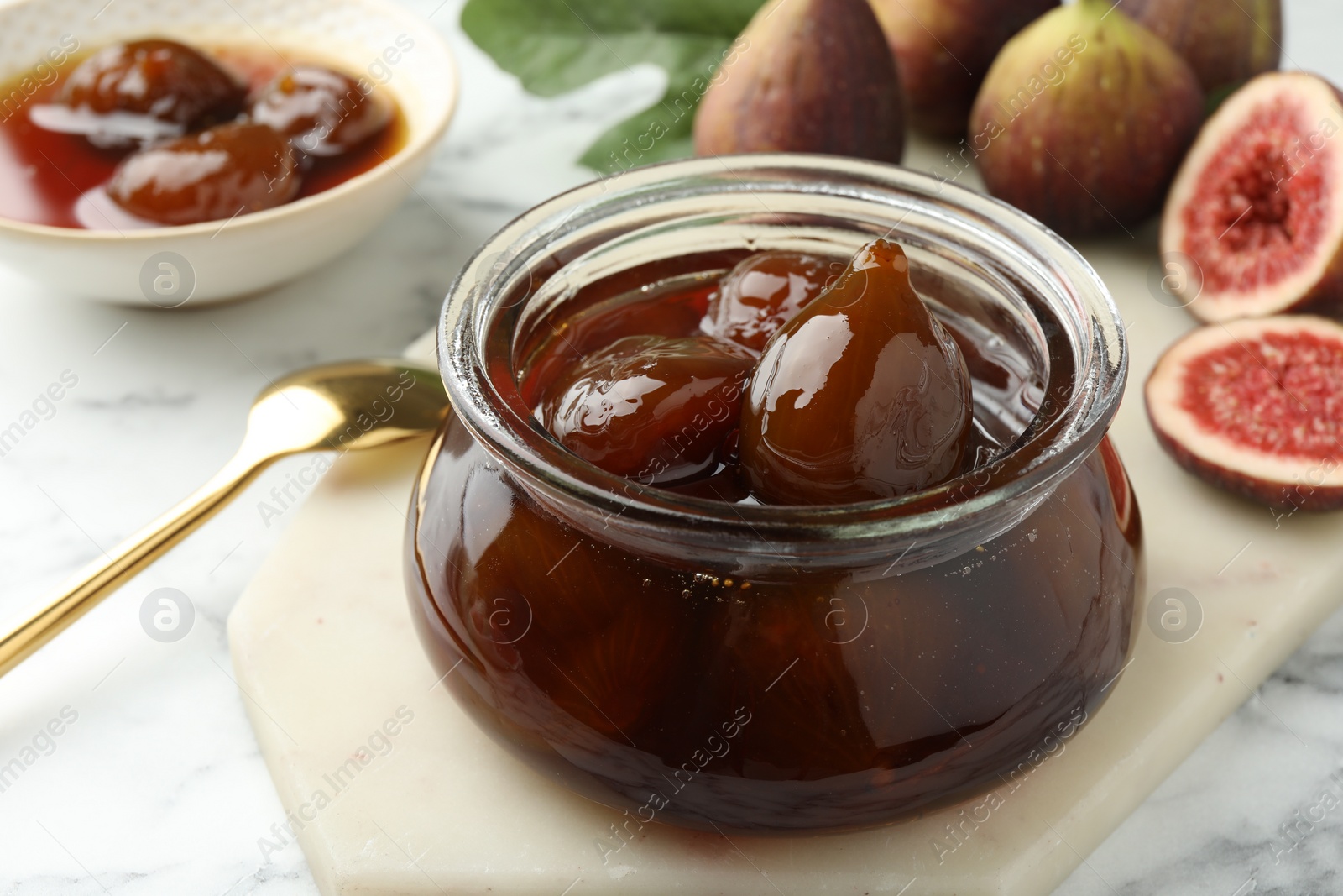 Photo of Jar of tasty sweet fig jam on white marble table, closeup