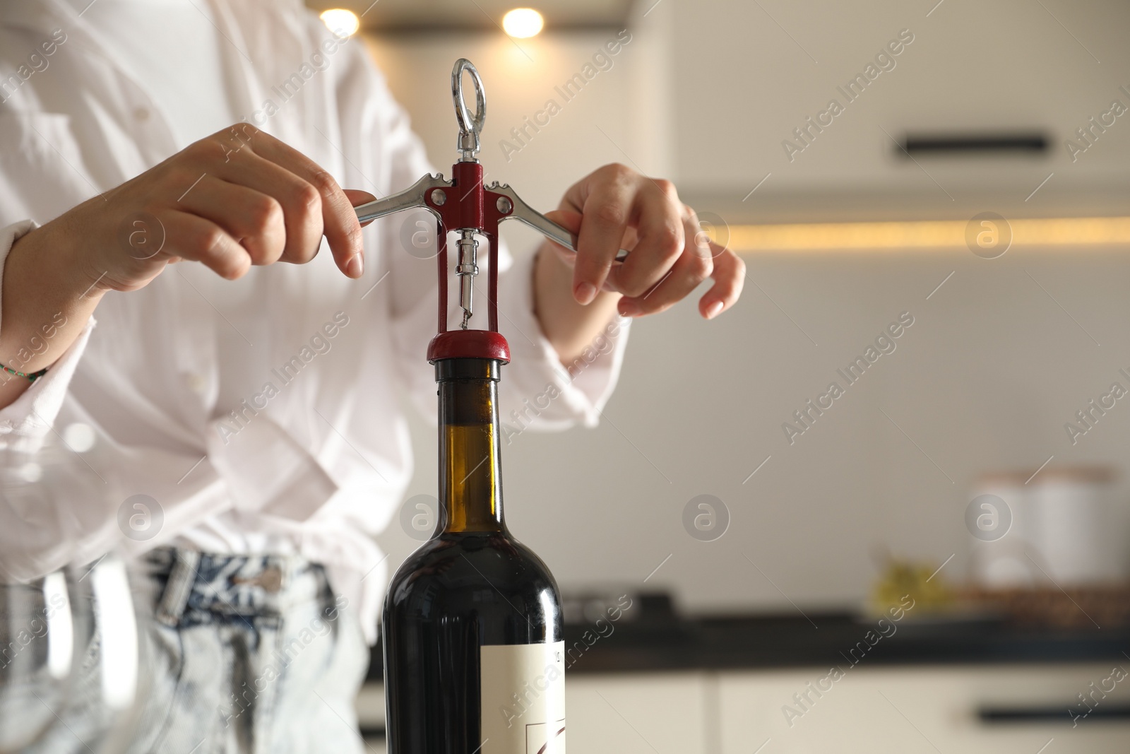 Photo of Woman opening wine bottle with corkscrew indoors, closeup. Space for text