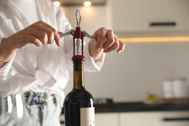 Photo of Woman opening wine bottle with corkscrew indoors, closeup. Space for text