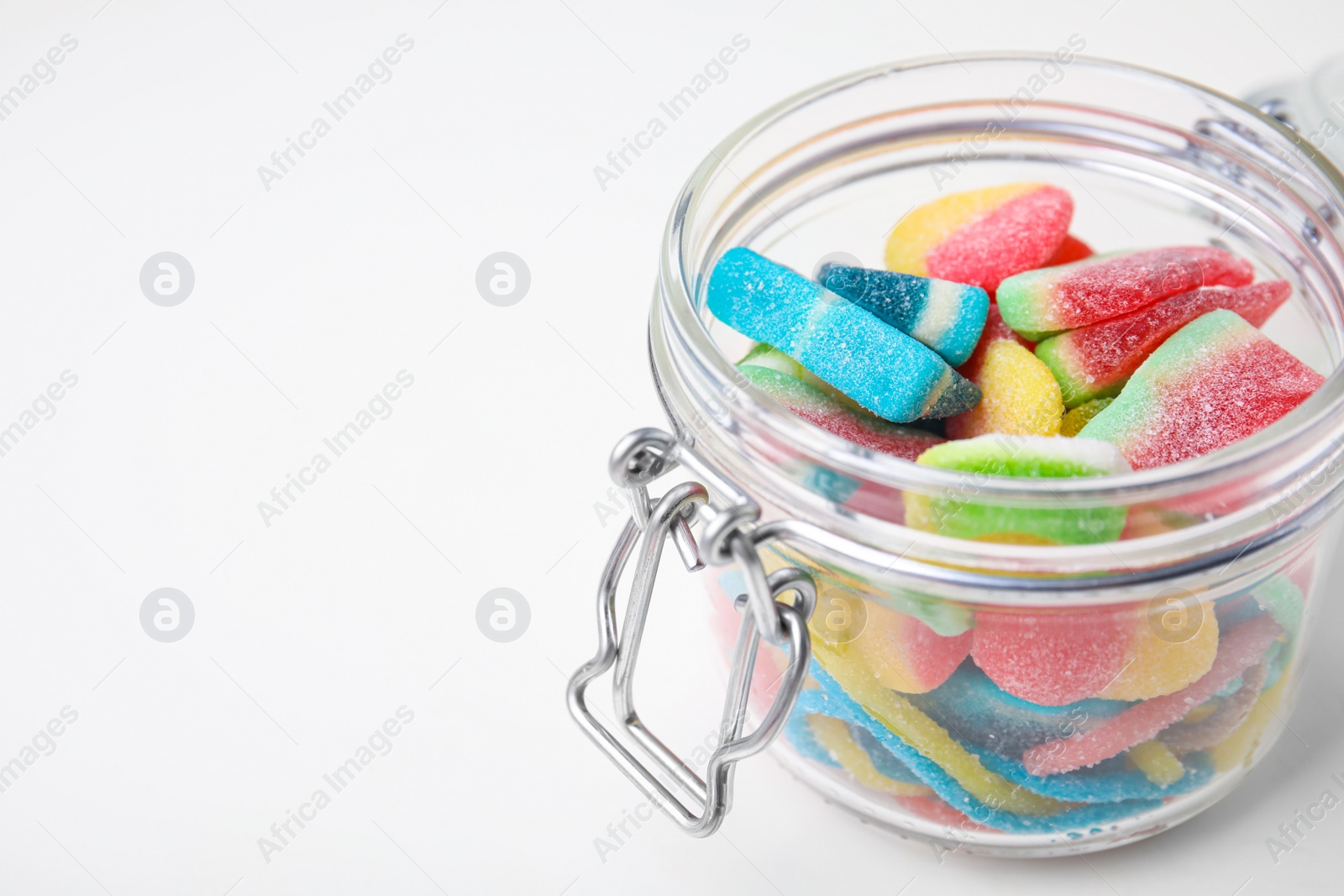 Photo of Tasty jelly candies in open jar on white table, closeup. Space for text