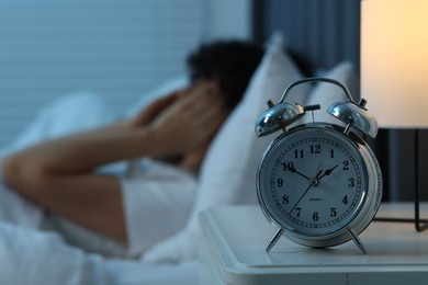 Woman suffering from headache in bed at night, focus on alarm clock