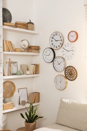 Photo of Stylish room interior with comfortable sofa, wall shelves and collection of clocks