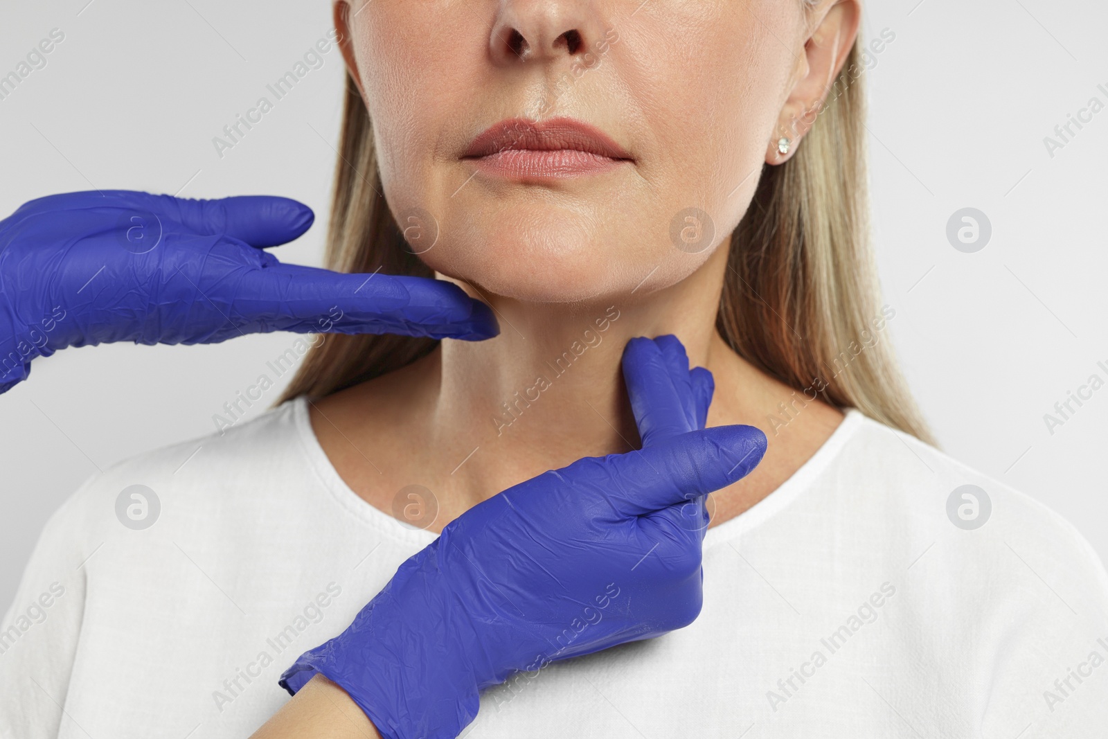 Photo of Endocrinologist examining thyroid gland of patient on light grey background, closeup