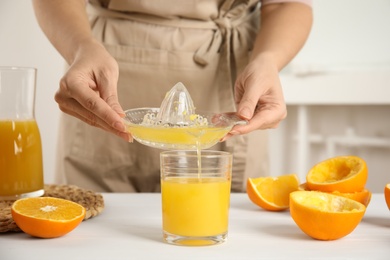 Photo of Woman pouring freshly made orange juice in glass at white table, closeup