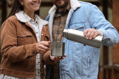 Photo of Boyfriend pouring hot drink from metallic thermos into cup for his girlfriend outdoors, closeup