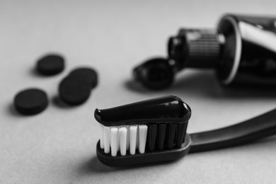 Photo of Brush with charcoal toothpaste on light grey background, closeup