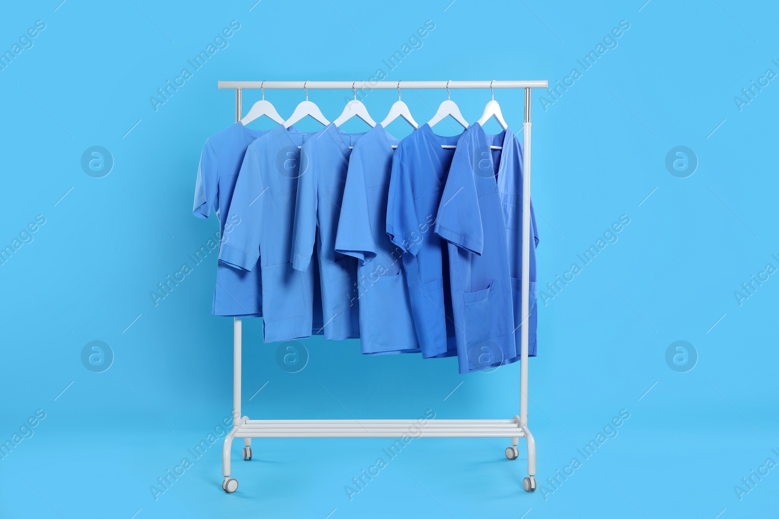 Photo of Medical uniforms on rack against light blue background