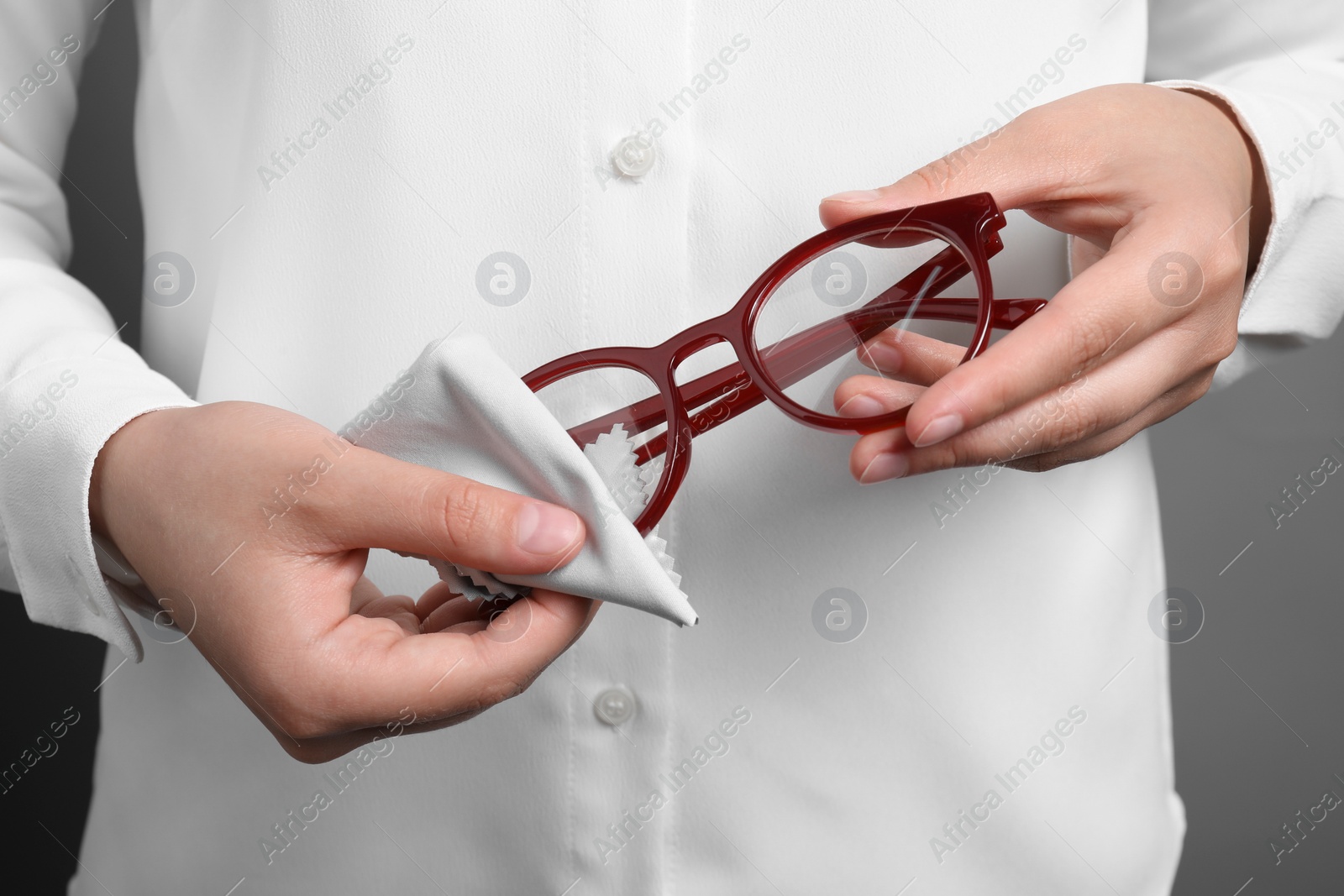 Photo of Woman wiping her glasses with microfiber cloth on grey background, closeup