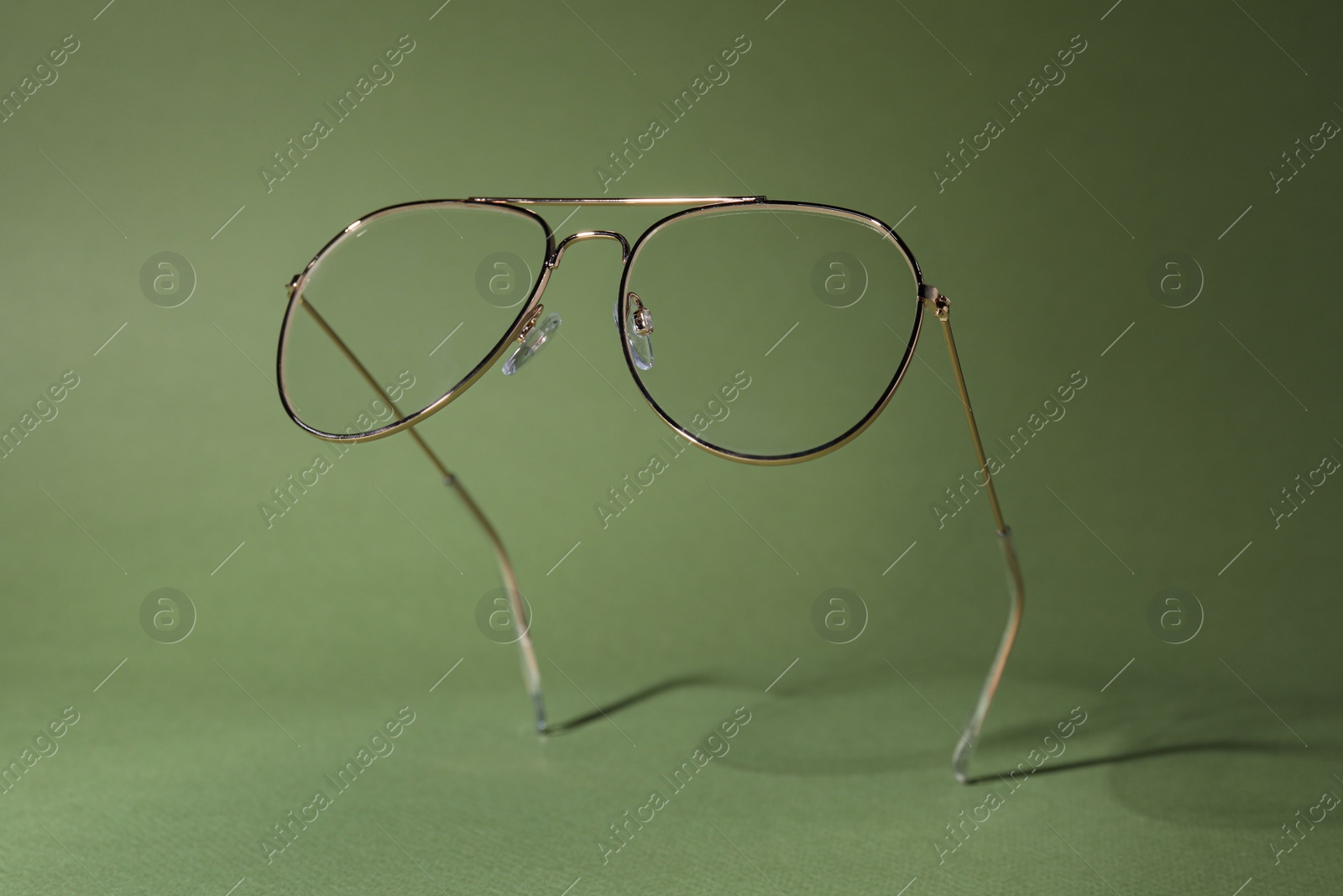 Photo of Stylish pair of glasses with metal frame on olive background