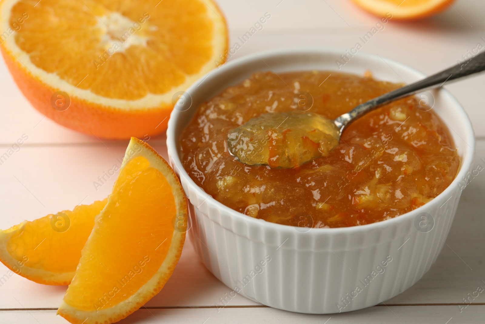 Photo of Delicious orange marmalade in bowl with spoon on white wooden table, closeup