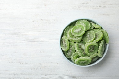 Photo of Bowl of dried kiwi on wooden background, top view with space for text. Tasty and healthy fruit