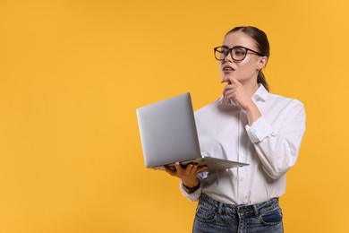 Photo of Thoughtful woman in glasses with laptop on orange background. Space for text