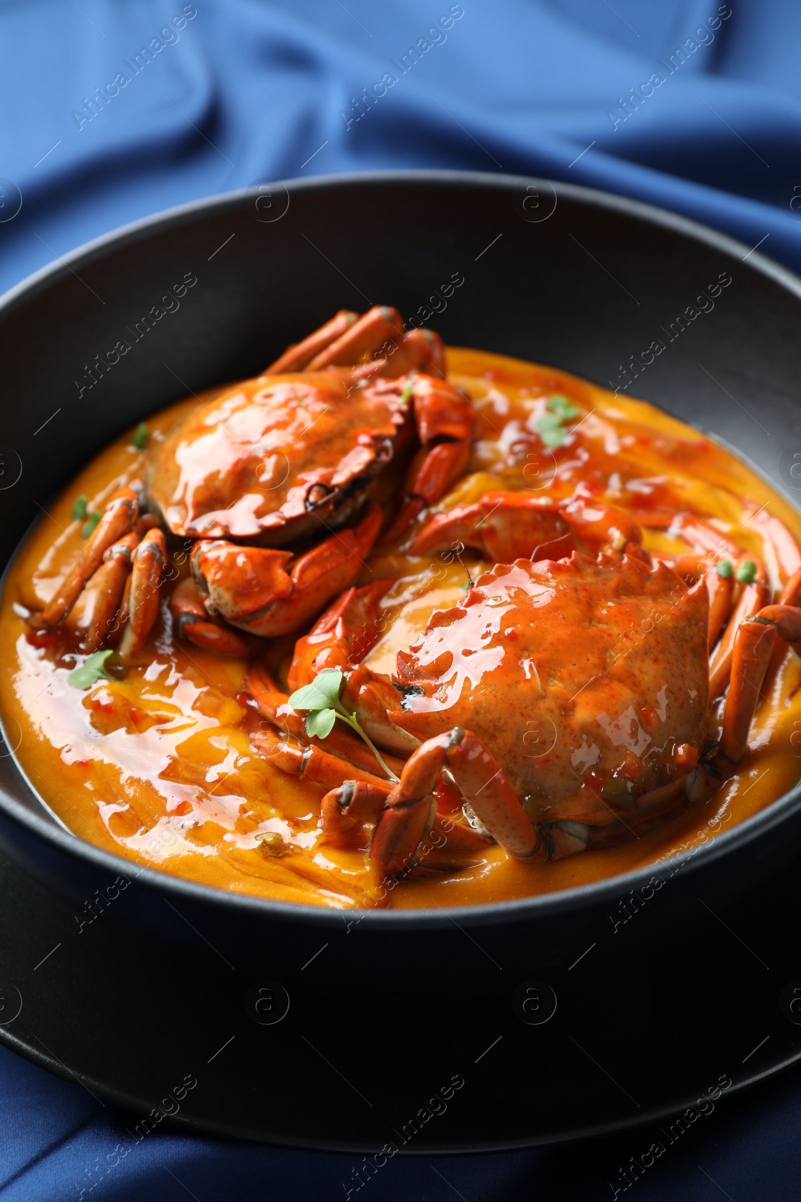 Photo of Delicious boiled crabs with sauce in bowl on blue tablecloth