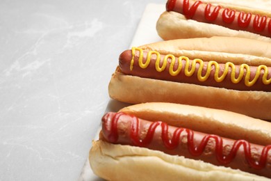 Photo of Fresh delicious hot dogs with sauces on light grey marble table, closeup. Space for text