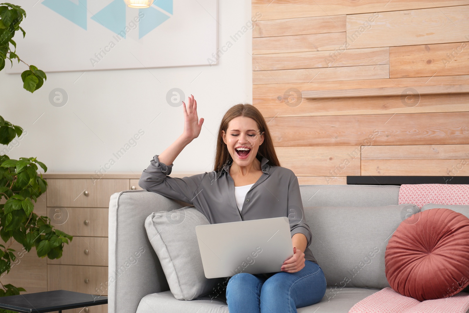 Photo of Emotional young woman with laptop celebrating victory on sofa at home