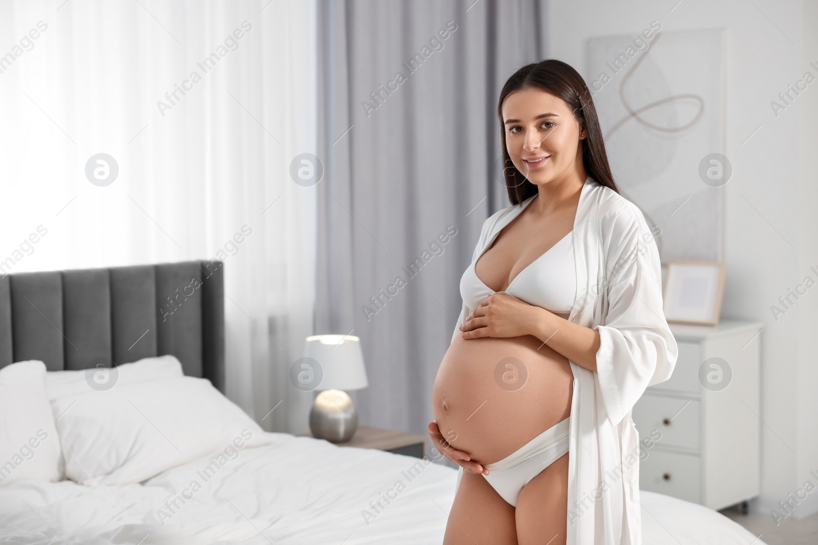 Photo of Beautiful pregnant woman wearing stylish comfortable underwear and robe in bedroom, space for text