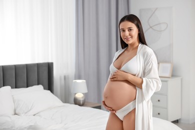 Beautiful pregnant woman wearing stylish comfortable underwear and robe in bedroom, space for text