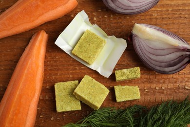 Photo of Bouillon cubes and other ingredients for soup on wooden table, flat lay