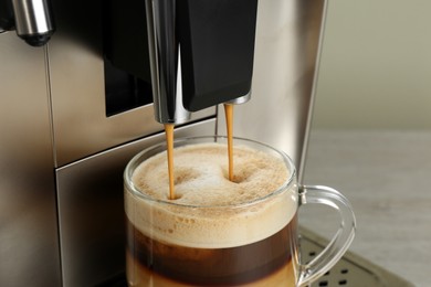 Photo of Modern coffee machine making latte into glass cup on wooden table, closeup