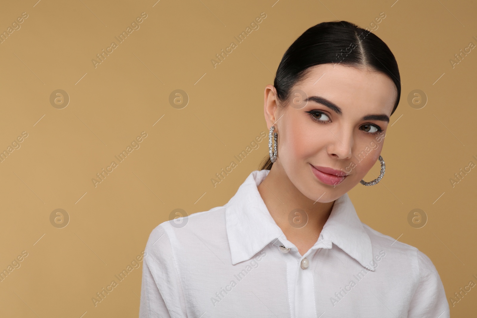 Photo of Beautiful young woman with elegant earrings on beige background. Space for text