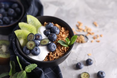 Photo of Tasty granola with yogurt, blueberries and kiwi in bowl on gray table, closeup