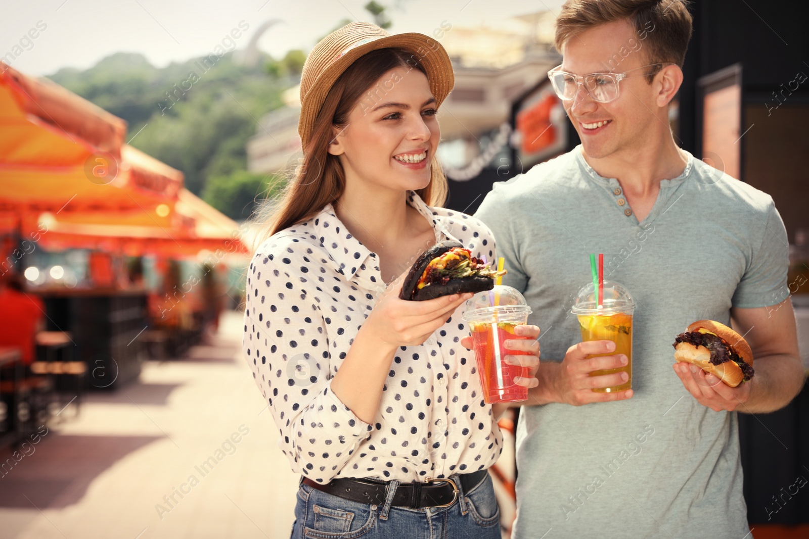 Photo of Young happy couple with burgers walking on city street