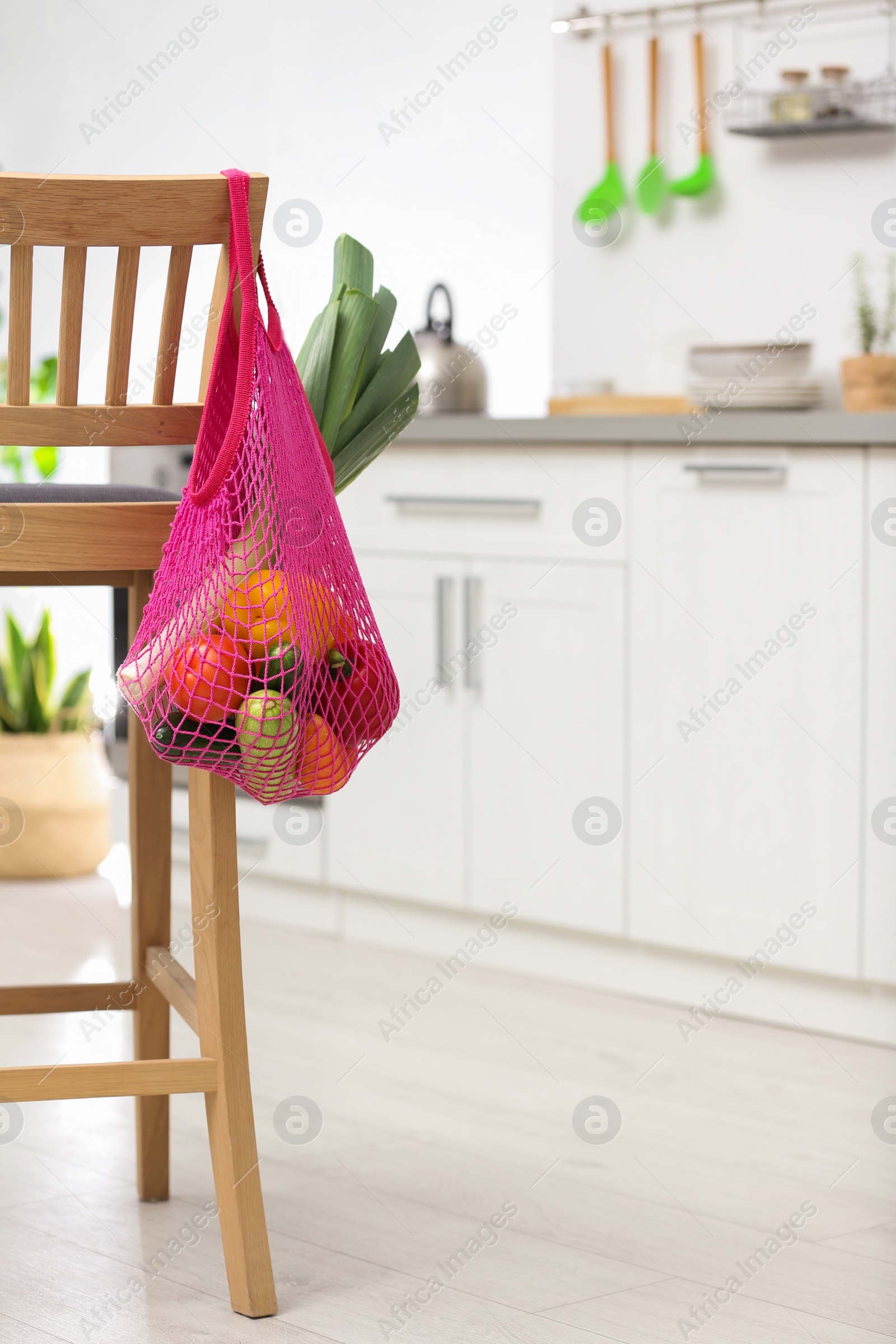 Photo of Net bag with vegetables hanging on wooden chair in kitchen