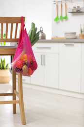 Net bag with vegetables hanging on wooden chair in kitchen