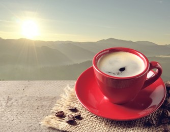 Cup of aromatic hot coffee on wooden table and beautiful view of mountain landscape. Space for text