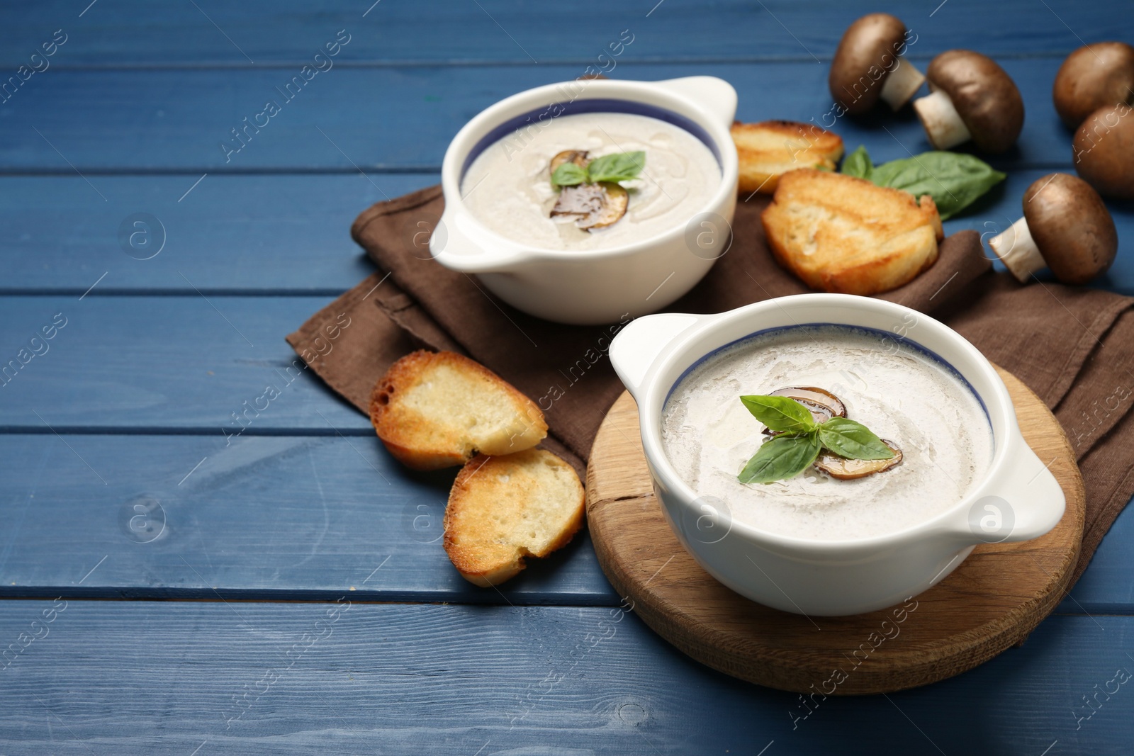 Photo of Delicious mushroom soup in ceramic pots and fresh ingredients on blue wooden table. Space for text