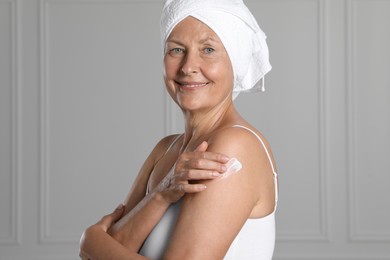 Happy woman applying body cream onto shoulder near white wall