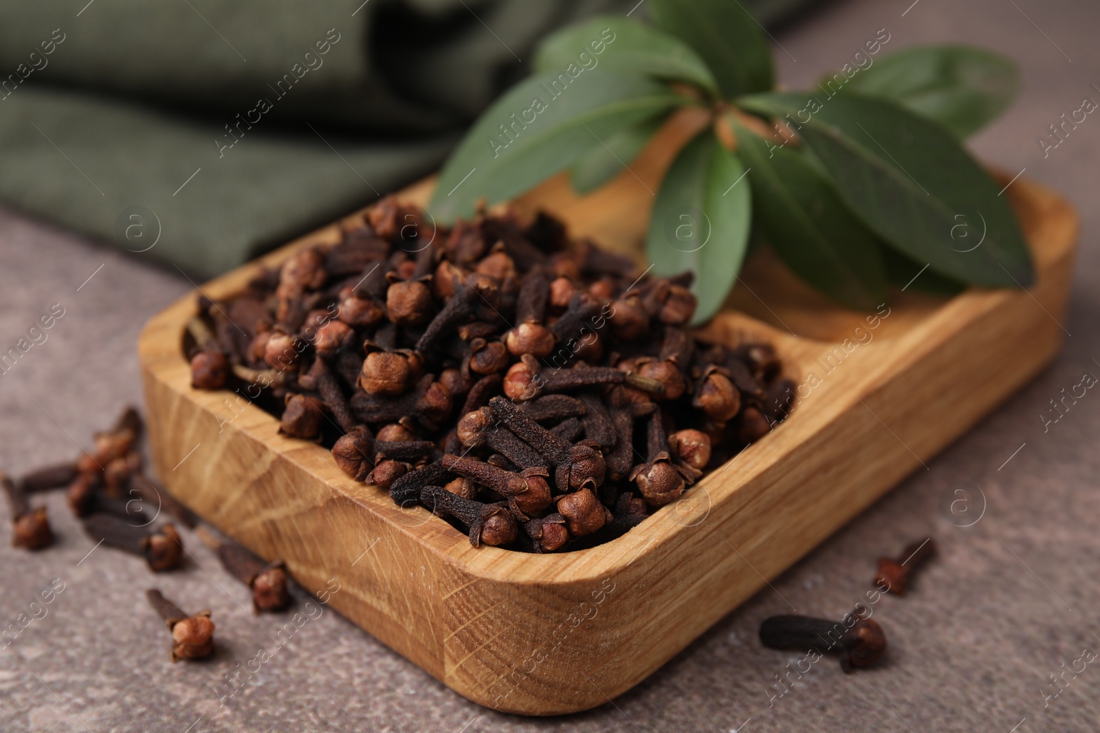 Photo of Wooden tray with aromatic cloves and green leaves on brown table, closeup