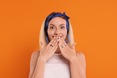 Photo of Portrait of surprised hippie woman covering mouth on orange background