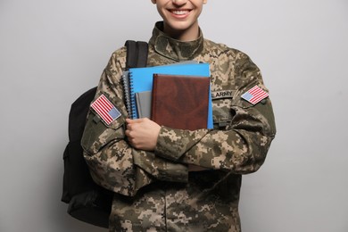 Female cadet with backpack and notebooks on light grey background, closeup. Military education
