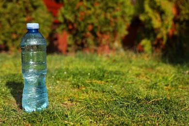Photo of Plastic bottle of water on green grass outdoors. Space for text