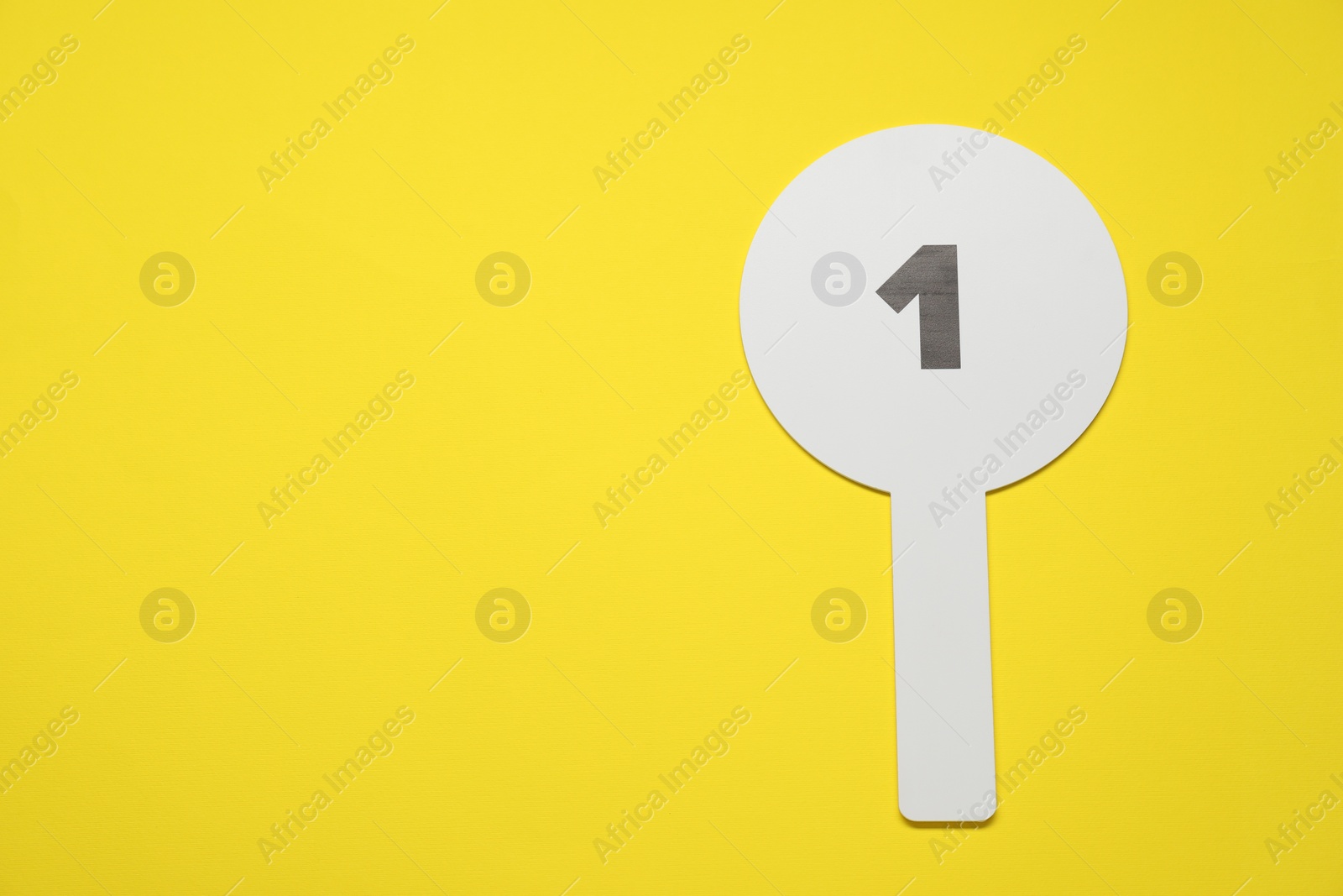 Photo of Auction paddle with number 1 on yellow background, top view. Space for text