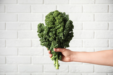 Photo of Woman holding fresh kale leaves near white brick wall, closeup