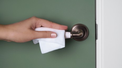 Woman cleaning doorknob with wet wipe indoors, closeup. Protective measures