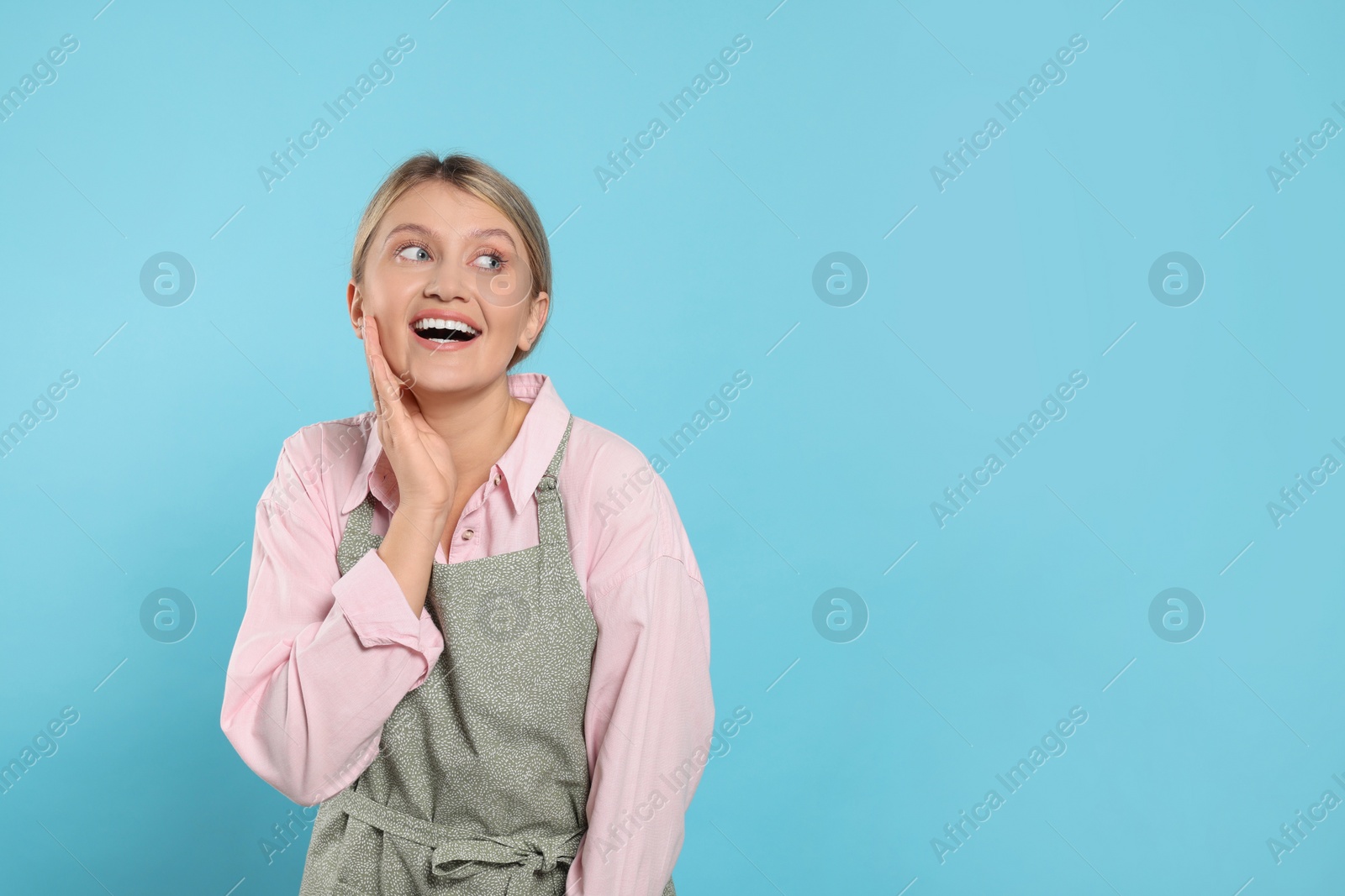 Photo of Beautiful young woman in clean apron with pattern on light blue background. Space for text