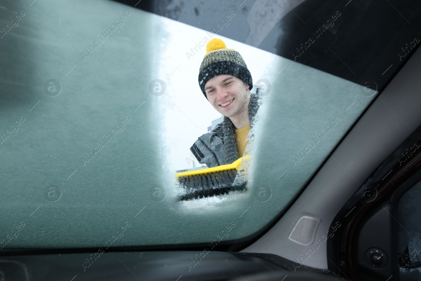 Photo of Man cleaning snow from car windshield, view from inside