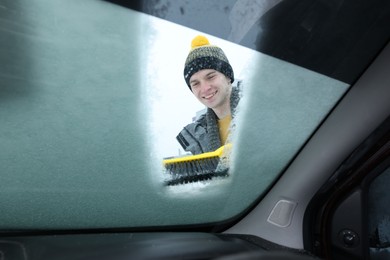 Man cleaning snow from car windshield, view from inside