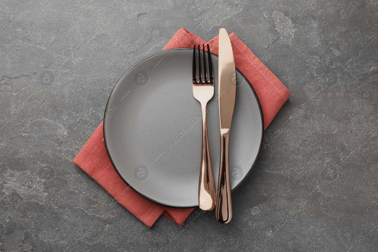 Photo of Clean plate, cutlery and napkin on grey textured table, top view