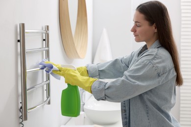 Woman cleaning heated towel rail with sprayer and rag